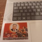 The second photo of Colwell's laptop, displaying the interior keyboard. It includes two decals of North Korea dictator Kim Il Sung's official posthumous portrait, including one of a mural depicting him as the sun shining upon the people of North Korea.