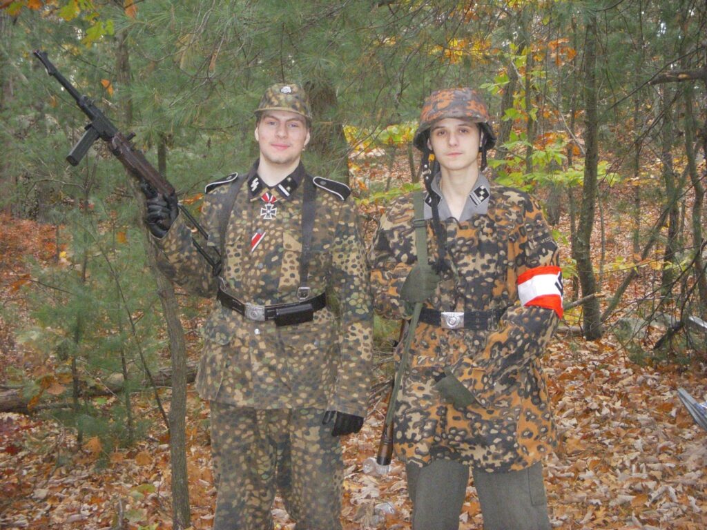 Beaudry in the woods around Weymouth MA, dressed in a full camo Nazi military uniform with Hauptsturmführer-rank patches. He is with Daniel Beaudry, his brother, also in a camo Nazi military uniform with Hauptscharführer-rank patches, whose face I will not be redacting.