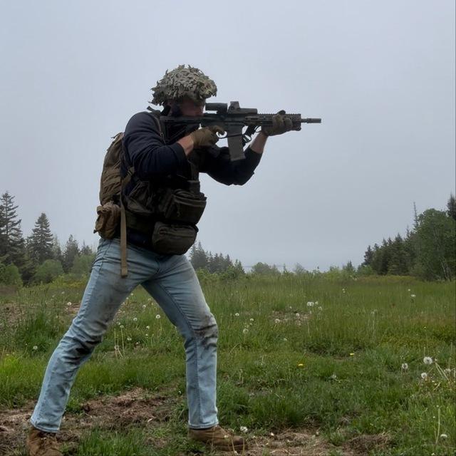 A photo of who is apparently Brandon Brooks, dressed in a tactical vest and practicing with what appears to be a carbine rifle.
