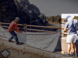 A photo of two white men dropping a banner from an overpass in Cromwell CT during October 2024. One of them, highlighted, wears what appear to be white shorts, a navy blue shirt, black Adidas trainers, and a white half-face gaiter. He has dark hair.