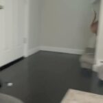 Another still of the video posted by Behling to the Silver Stackers Telegram chat on September 2nd, 2024. We see what is to the right of the background in the previous still: dark hardwood or veneered floors, a white door, white moulding, and a carpeted stairwell up concealed by a wall, and a base heater. An orange tabby is visible scampering up the stairwell.