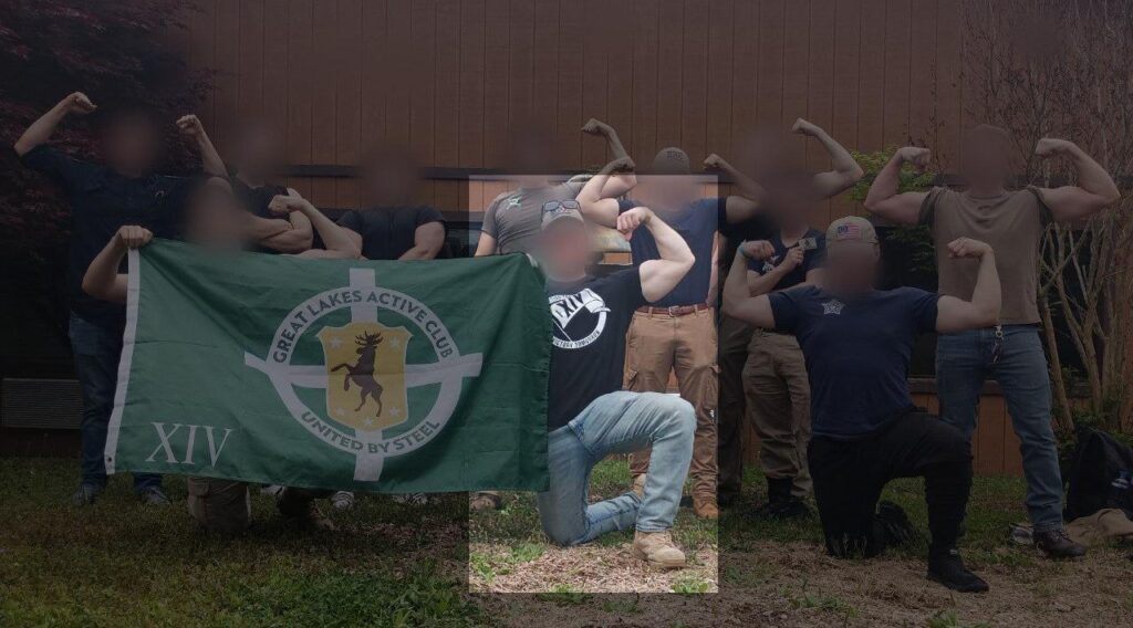 A photo of various Active Club members, all white men with blurred faces, posing with a Great Lakes AC flag sometime during or before May 2024. One member, on one knee, flexes his left bicep while holding a corner of the AC flag. His right arm is occluded by the flag itself. he wears a XIV-themed Will2Rise Active Club t-shirt. The XIV, of course, hearkens to the neo-Nazi "14 words" slogan.