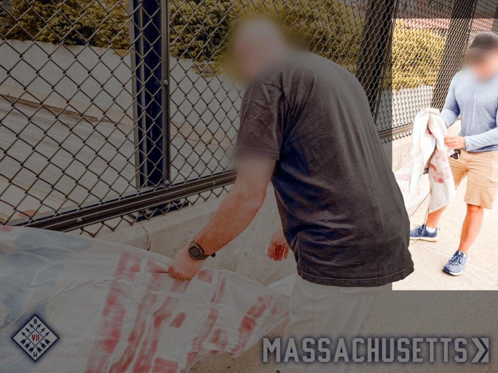 A photo of Patriot Front members preparing to drop a banner from an overpass somewhere in Worcester MA, during or before June 2025. One man in the background, his hands full of banner, appears to be Garrett Berna. He wears the same outfit he did while putting up Patriot Front posters in September 2024.